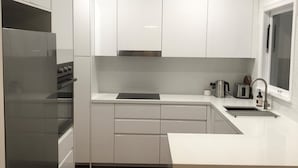 A modern kitchen with white cabinets, a stainless steel refrigerator, and a built-in oven. - Centrally located "Bargara Beach Cottage" (Bargara)