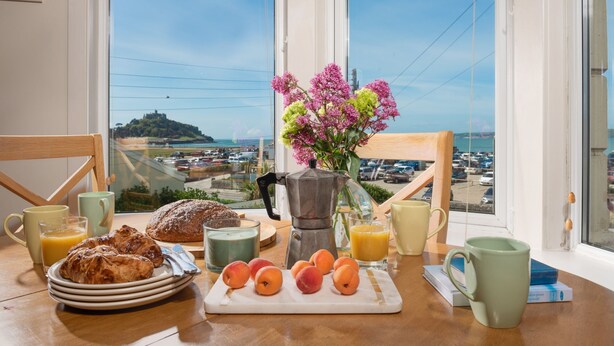 Una tavola imbandita con pasticcini, frutta e bevande, con vista su un parcheggio e una collina in lontananza.