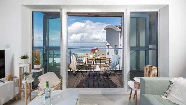 Ein modernes Wohnzimmer mit einer großen Schiebetür zu einem Balkon mit Meerblick.