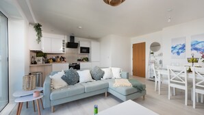 Ein modernes Wohnzimmer mit einem hellblauen Sofa, einem Essbereich mit weißer Möbel und einer Küche im Hintergrund.
