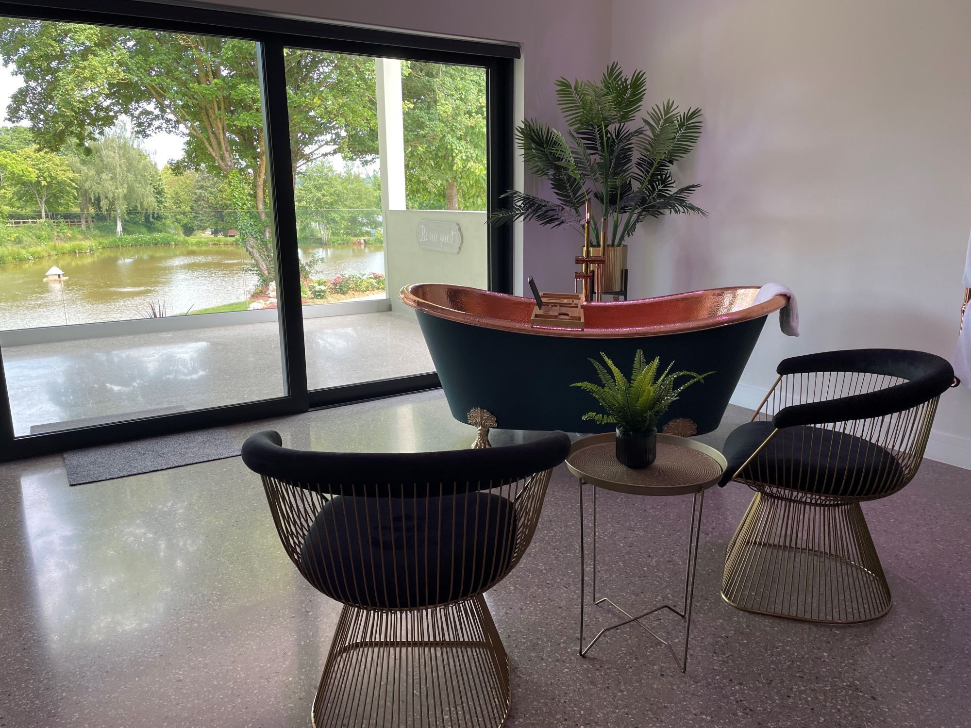 A modern room with a large window, a bathtub, two chairs, and a small table.
