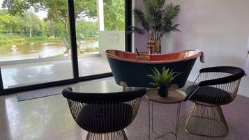A modern room with a large window, a bathtub, two chairs, and a small table.