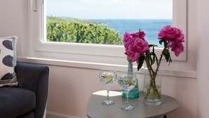Una habitación con vista al mar, una mesa con dos vasos y un jarrón de flores.