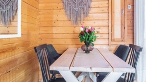 Ein Holzinterieur mit Tisch und Stühlen, einem Wandbehang aus Makramee und einer Vase mit Blumen.