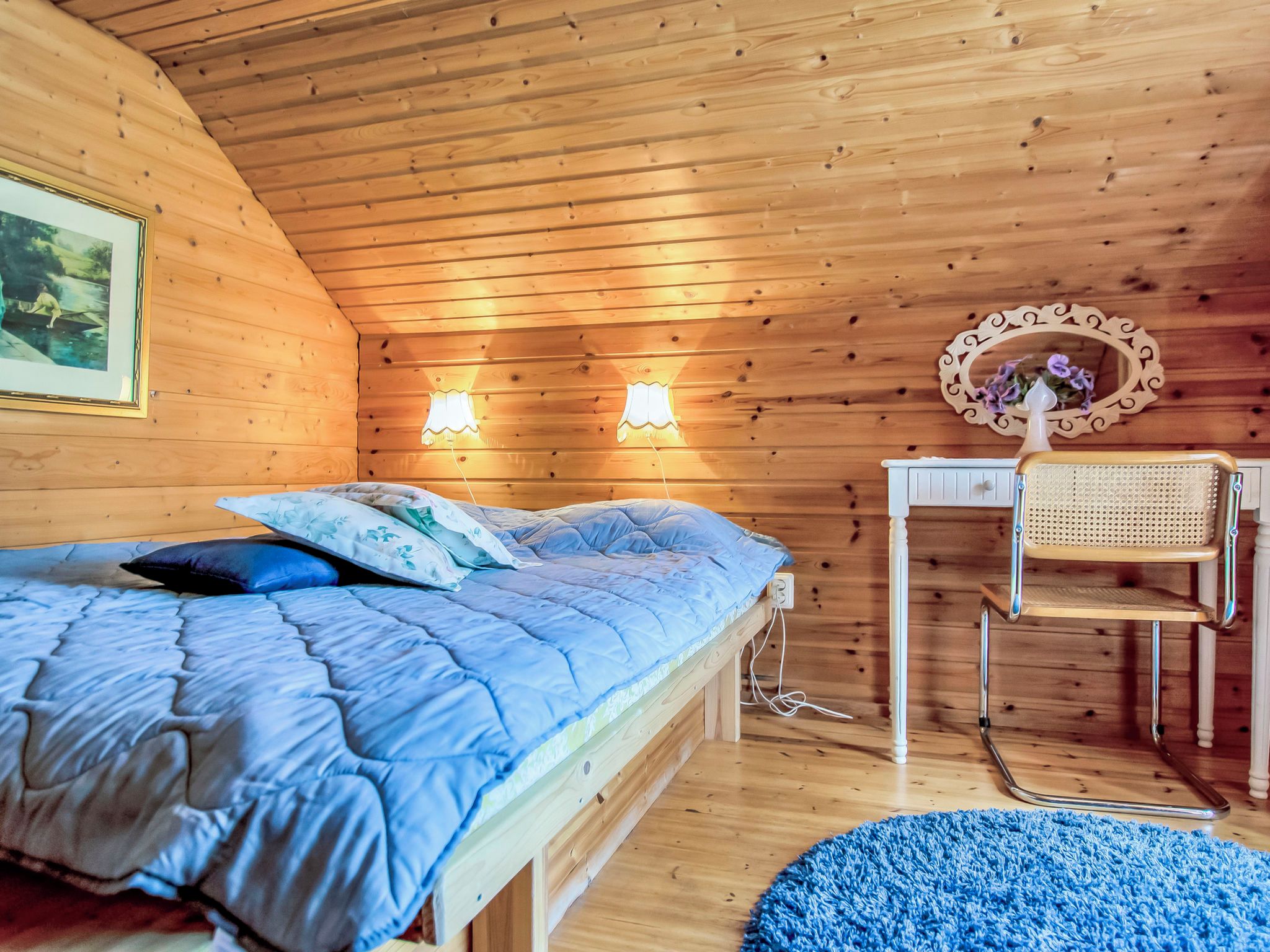A wooden room with a bed, two wall-mounted lights, a chair, a mirror, and a picture on the wall.