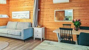 Ein gemütliches Blockhaus-Interieur mit einer Couch, einem Esstisch, Stühlen, einem kleinen Schrank und einem Deckenventilator.