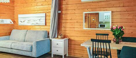 Interior acogedor de una cabaña con sofá, mesa de comedor, sillas, un mueble bajo y un ventilador de techo.