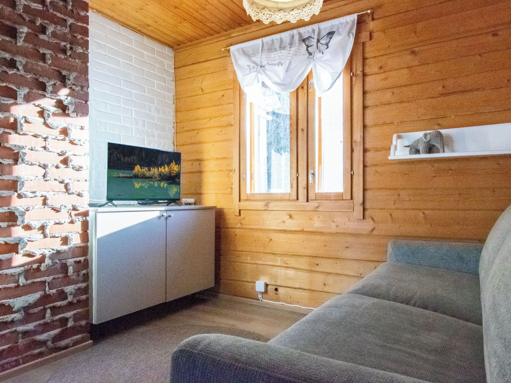 A wooden interior with a TV on a cabinet, a window with curtains, and a shelf with a small item.