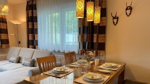Een eetgedeelte met een houten tafel voor vier personen, omringd door een bank en gordijnen.