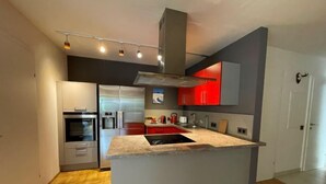 Een moderne keuken met een centraal eiland, roestvrijstalen apparatuur en rode kastjes.