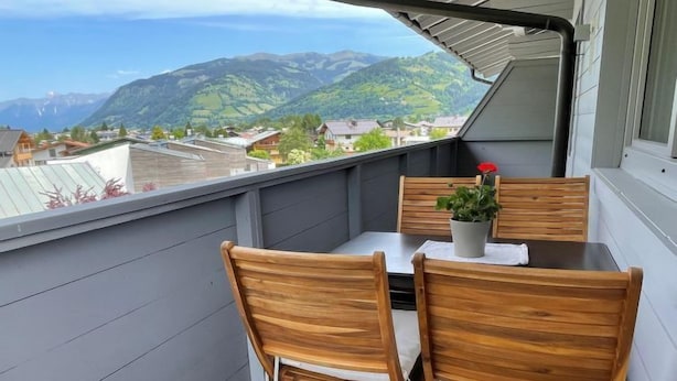 Een balkon met een tafel en twee stoelen, een bloempot en uitzicht op een bergachtig landschap.