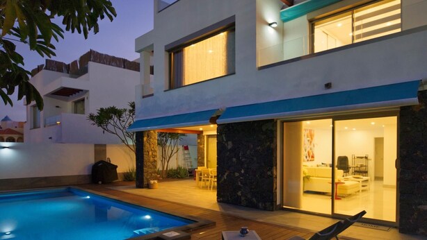 Ein modernes, zweistöckiges Haus mit Pool, Sitzgelegenheit im Freien und einem hellen Innenraum.