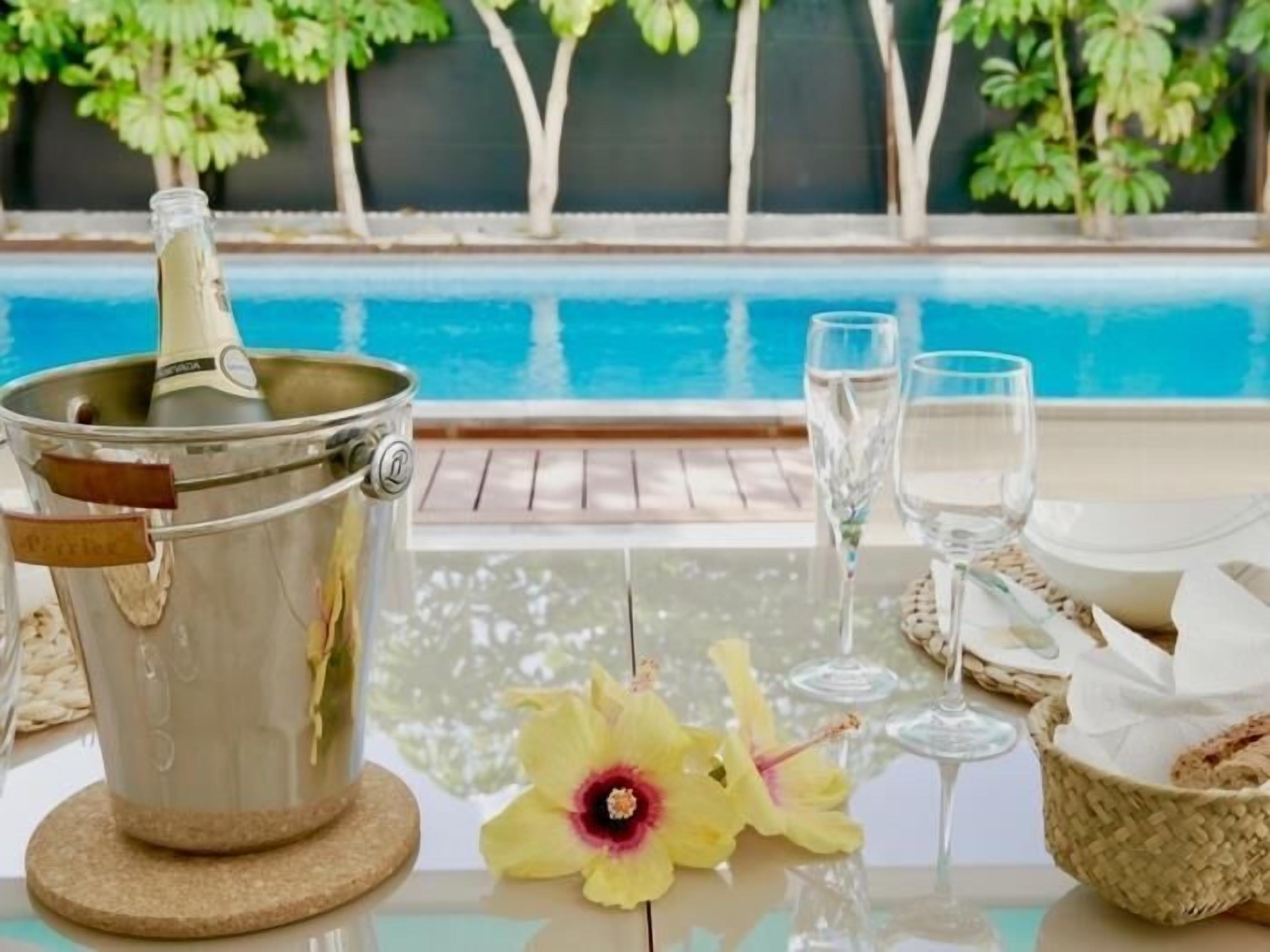 Ein Poolbereich mit einer Champagnerflasche in einem Metallkübel, zwei Gläsern, einer Blume und einem Korb auf einem Tisch.
