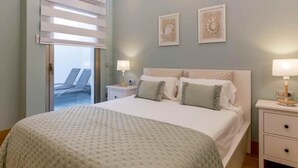 Ein Schlafzimmer mit einem großen Bett, zwei Nachttischen mit Lampen und Blick auf einen Balkon.