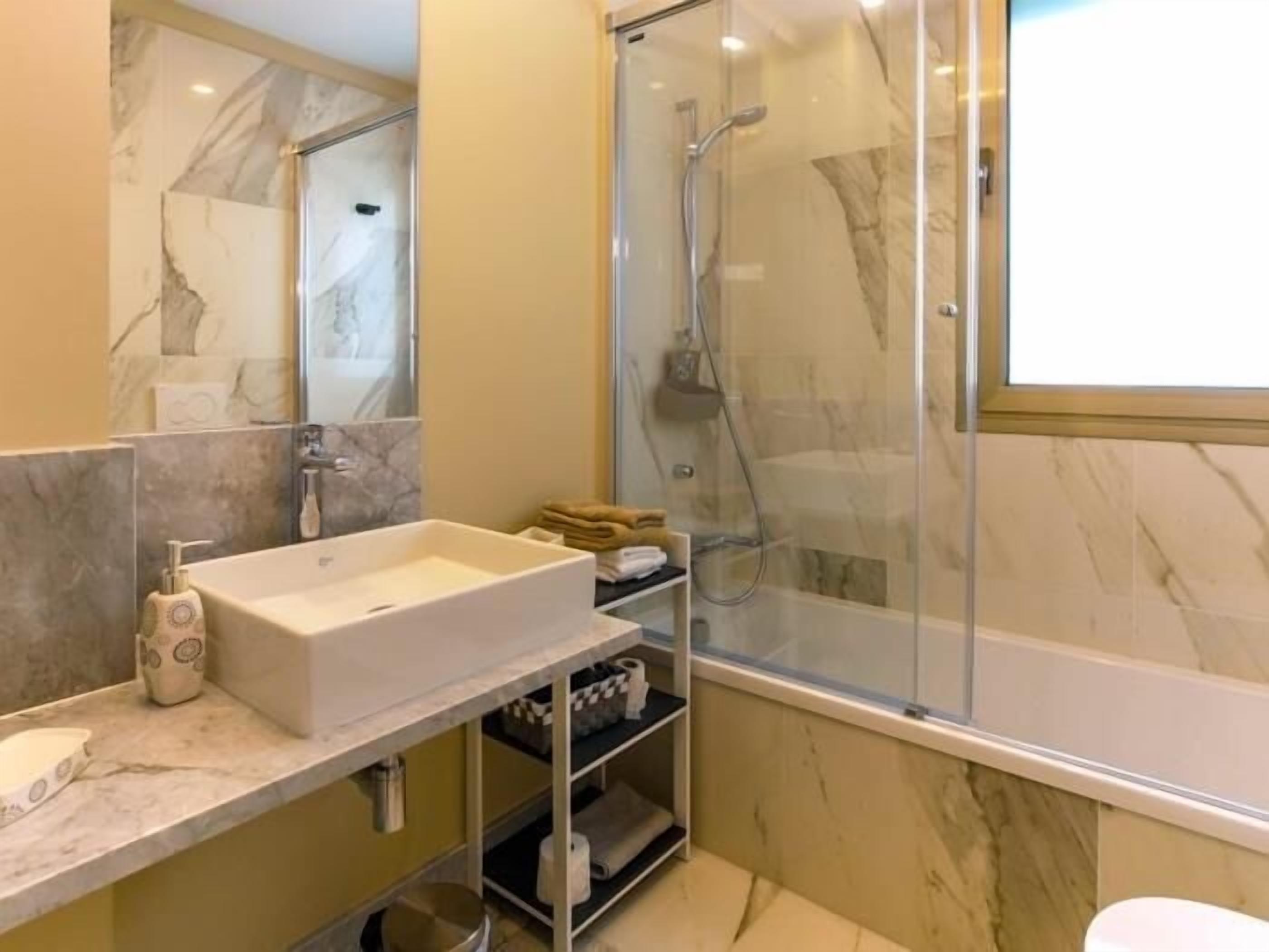 A modern bathroom with a marble sink, a glass-enclosed shower, and a mirror above the sink.