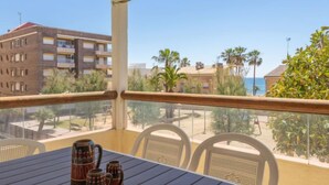 Un balcon avec une table et des chaises, donnant sur une plage et des immeubles.