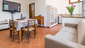 Una sala de estar con sofá, una mesa de comedor con sillas, un televisor montado en la pared y un mueble con puertas de cristal.