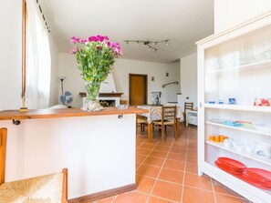 A kitchen with a wooden counter, a dining area with a table and chairs, and a shelf with kitchenware.