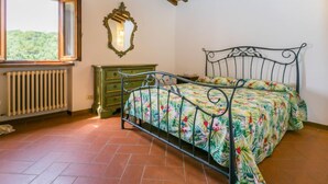 Un dormitorio con cama, cómoda, radiador, ventana con vistas y techo con vigas y luces de madera.