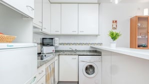 Una cocina compacta con armarios blancos, lavadora, microondas y tostadora.