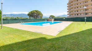 Una piscina con vistas despejadas a montañas al fondo, rodeada de un césped cuidado y un edificio de varios pisos.