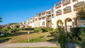 A multi-story hotel with balconies, a well-maintained garden, and a clear blue sky. - L'Esquinade P1 111 by Interhome (Agay Village Cap Esterel)
