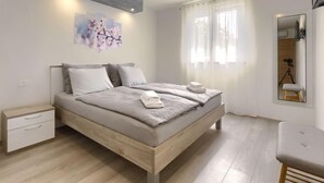 Une chambre à coucher moderne avec un lit en bois, du linge de lit blanc, une petite table de chevet et un grand miroir.