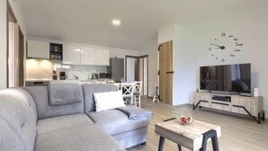 Un salon moderne avec un canapé d’angle gris, une table basse en bois et un téléviseur posé sur un meuble en bois.