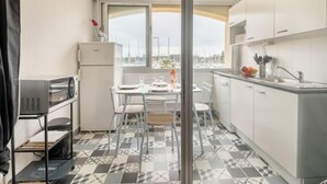 Een kleine keuken met een eethoek, een koelkast en een raam met uitzicht op boten.