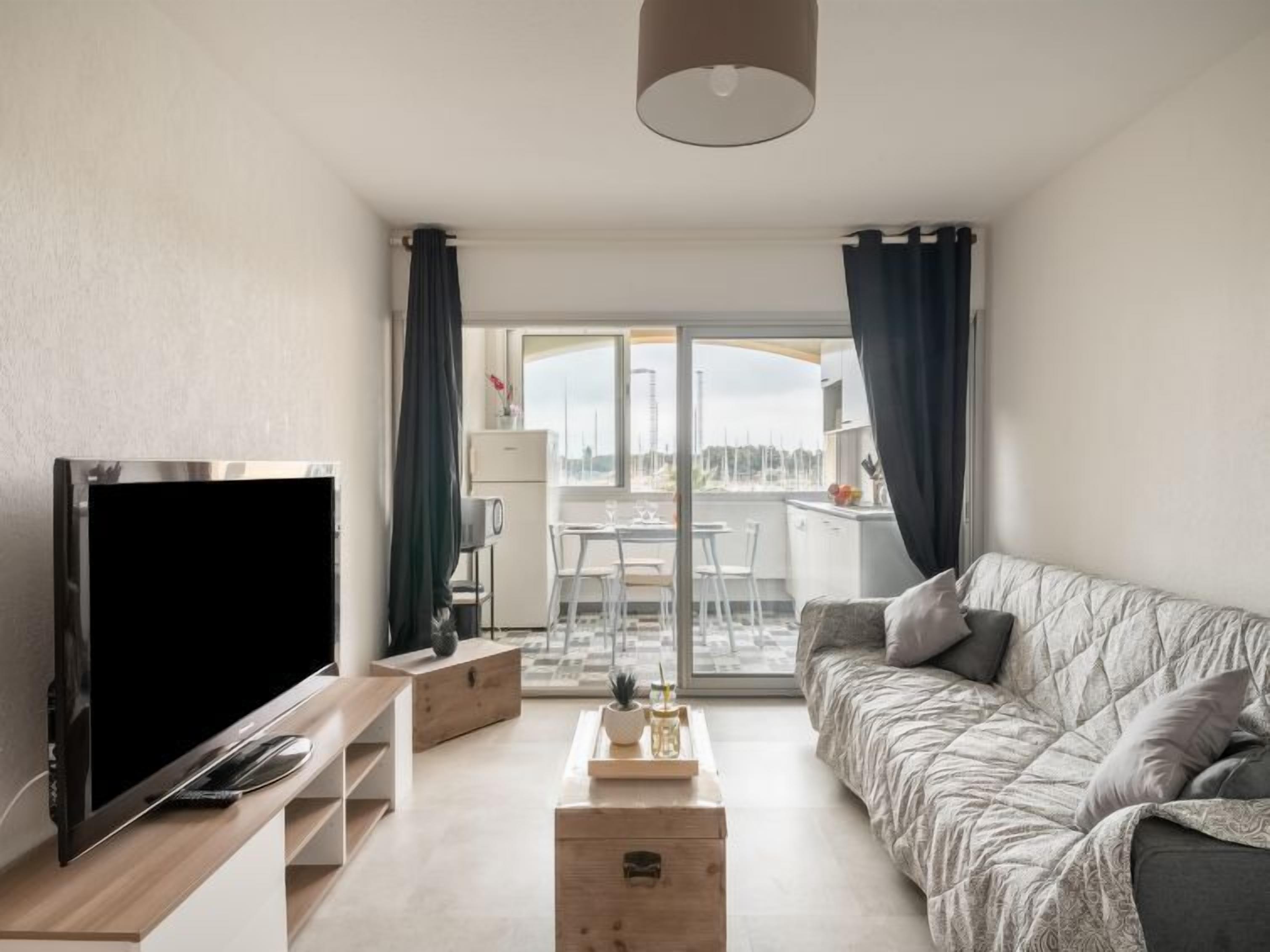 Uma sala de estar moderna com uma TV de tela plana, um sofá, uma mesa de centro e uma varanda com vista.