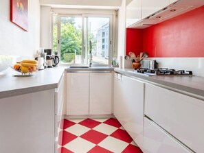 A modern kitchen with white cabinets, a red and white checkered floor, and a view of the outside through a glass door.