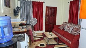 A compact living space with a red sofa, a small table, a water dispenser, a fan, and a door. - Cozy, comfortable, and beautiful apartment located in a safe gated community. (Georgetown)
