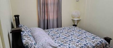 Een slaapkamer met een bed, nachtkastje, airconditioning aan de muur en een raam met gordijnen.