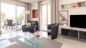Una sala de estar moderna con una mesa de centro de vidrio, un sofá negro, un sillón negro, un televisor de pantalla plana y una estantería.