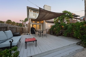 A covered patio with a table and chairs, a barbecue grill, and a sofa.