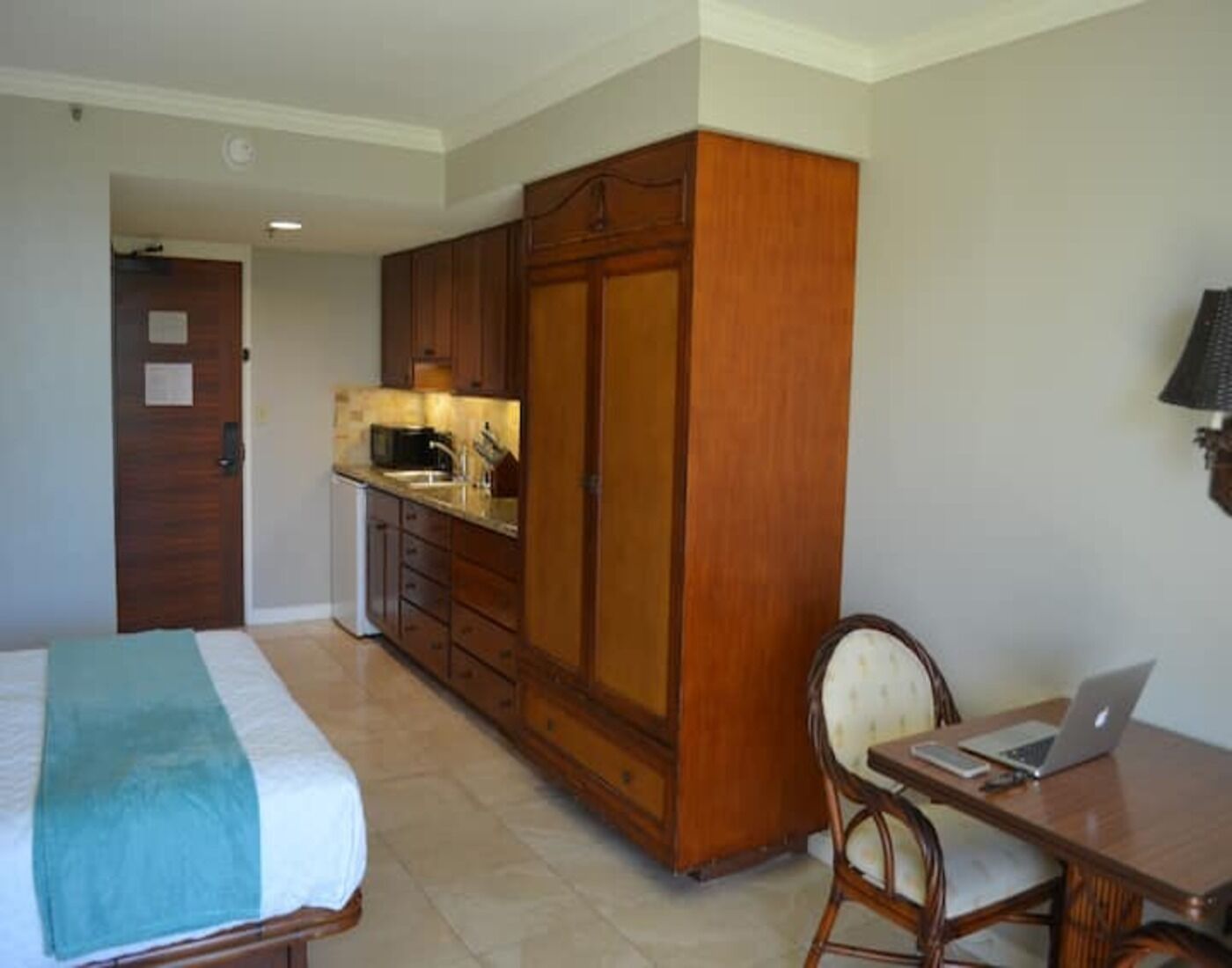 Une chambre d’hôtel comprenant un lit, un bureau avec un ordinateur portable, une armoire en bois et une kitchenette.