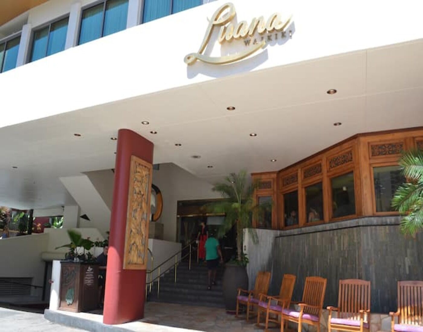 A hotel entrance with a sign reading "Pana," a staircase leading inside, and outdoor seating area with chairs.