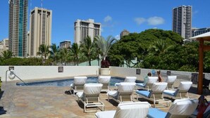 Un espace piscine aménagé sur le toit, avec des chaises longues et une vue sur les grands immeubles.