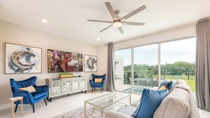 A spacious living room with a large window, a ceiling fan, and a modern sofa. - 3BR Reunion Townhome w/ Golf Views & Games (Kissimmee)