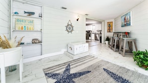 Uma sala de estar ampla com um tapete estampado em formato de estrela, um aparador branco e uma prateleira na parede com objetos decorativos.