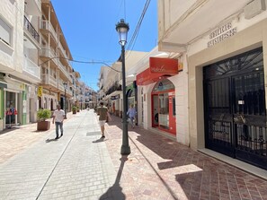 A pedestrian street lined with shops and buildings, including a red storefront with a sign that reads "Halconviajes.com".