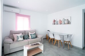 A modern living room with a sofa, coffee table, and dining area with chairs. - Centro Life Seaview by Casasol (Nerja)