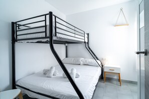 Ein Stockbett mit weißer Bettwäsche und Handtüchern, ein Nachttisch mit Lampe sowie eine Pendelleuchte.