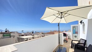 Une terrasse sur le toit, avec un grand parasol, une petite table et des chaises en osier noir.