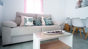 Un salon comprenant un canapé, deux fauteuils, une table basse et une fenêtre avec un store rose.