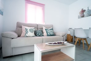 Ein Wohnzimmer mit einer Couch, zwei Sesseln, einem Couchtisch und einem Fenster mit rosa Jalousie.