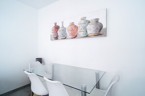 A modern bathroom with a glass shower enclosure, white chairs, and a wall-mounted artwork of vases.