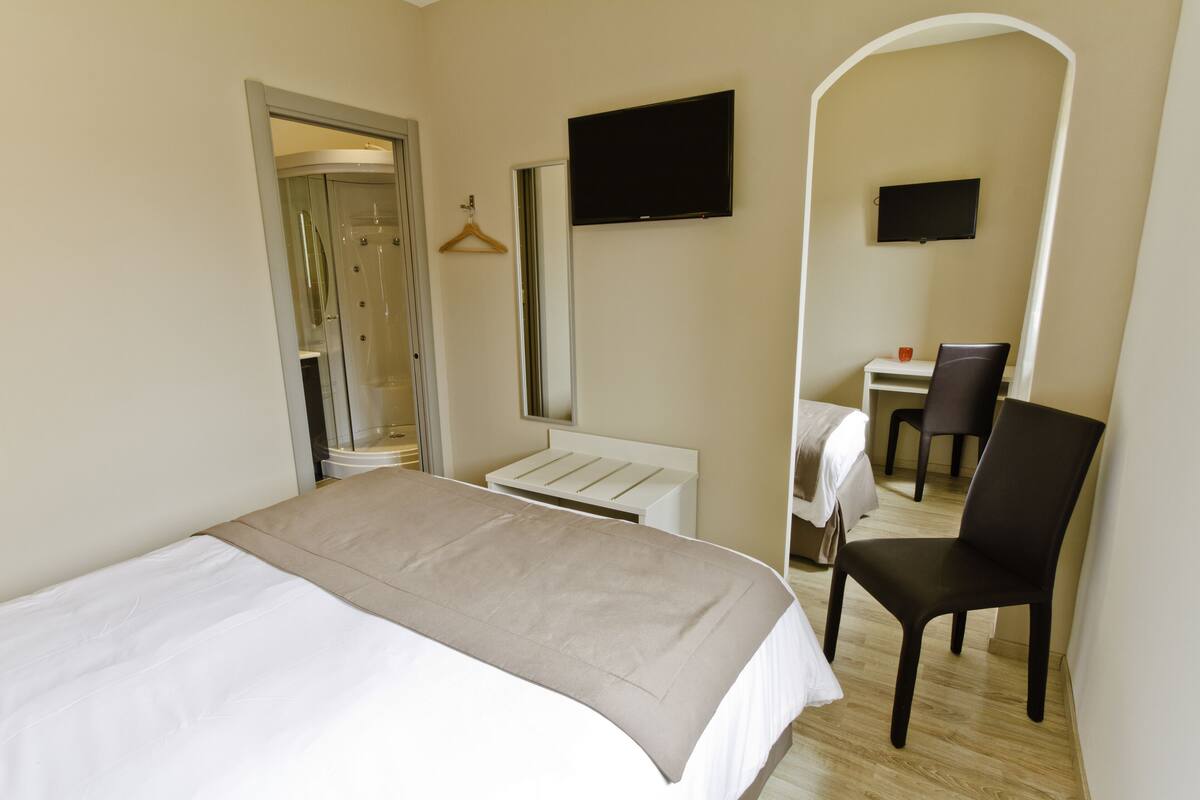 Una habitación de hotel con cama, escritorio, silla, televisor y espejo.