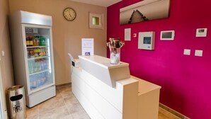 A reception area with a refrigerator stocked with beverages, a clock, and a vase on the counter. - Hôtel Les Petits Oreillers (Saint-Martin-d'Ardèche)