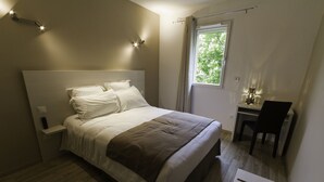 A bedroom with a bed, bedside table, and a desk with a chair. - Hôtel Les Petits Oreillers (Saint-Martin-d'Ardèche)